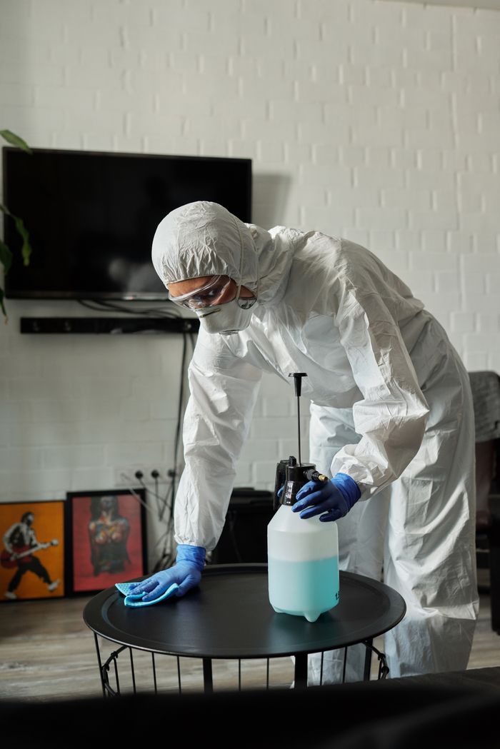 Person in protective gear cleaning a living room table with disinfectant.